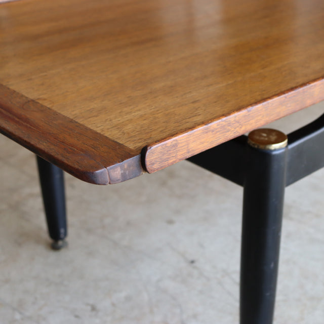 Vintage G-Plan mid-century teak coffee table corner with smooth wood grain and black tapered legs with brass caps.
