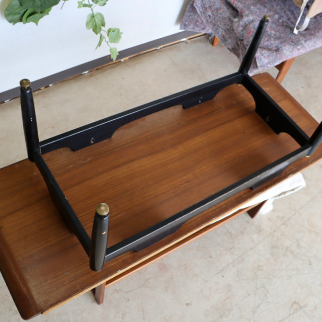 Vintage mid-century British G-Plan teak coffee table with visible wood grain and black tapered legs with brass caps, shown.