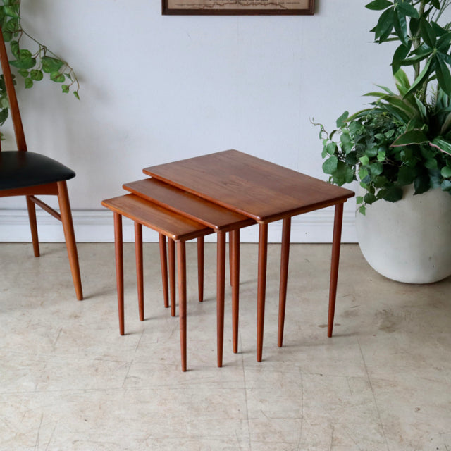 Set of three vintage mid-century Danish teak nest tables with slender tapered legs and smooth wood grain finish.