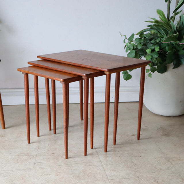Set of three mid-century Danish teak nest tables with sleek tapered legs and smooth wood grain finish, showcasing vintage.