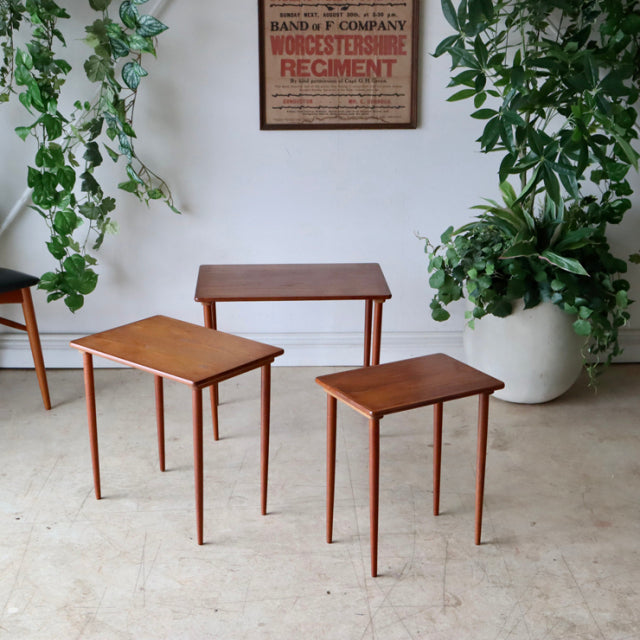 Set of three mid-century Danish teak nest tables with slender tapered legs and smooth wood grain finish, showcasing vintage.