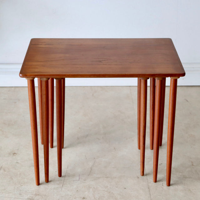 Vintage Danish teak nest tables with tapered mid-century legs and smooth wood grain surface.