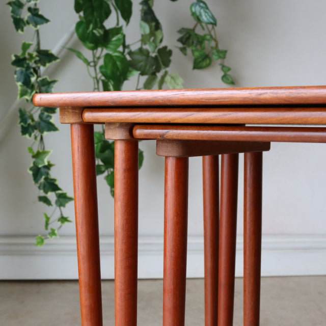 Set of vintage mid-century Danish teak nest tables with rounded edges and slender cylindrical legs showing natural wood grain.