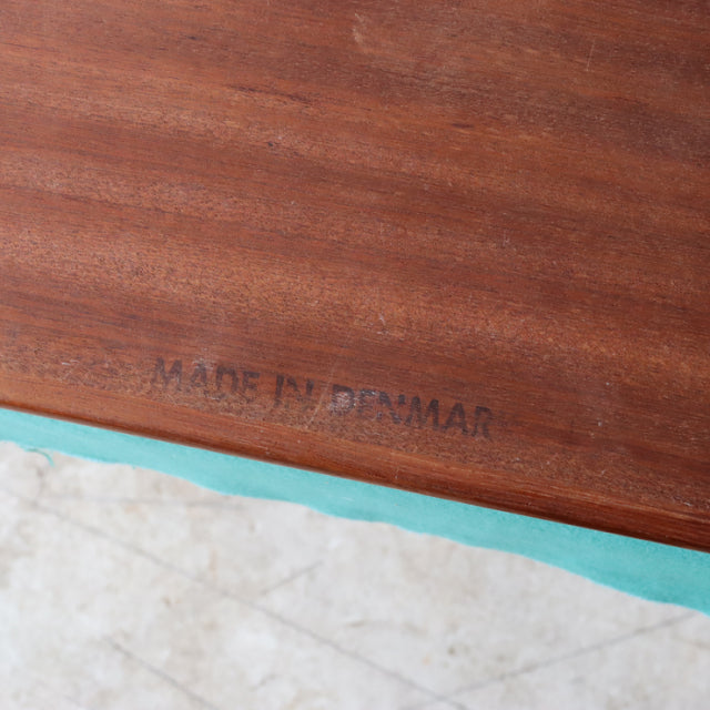 Close-up of mid-century teak wood with clear grain and "Made in Denmark" stamp on vintage British-Danish nest table surface.