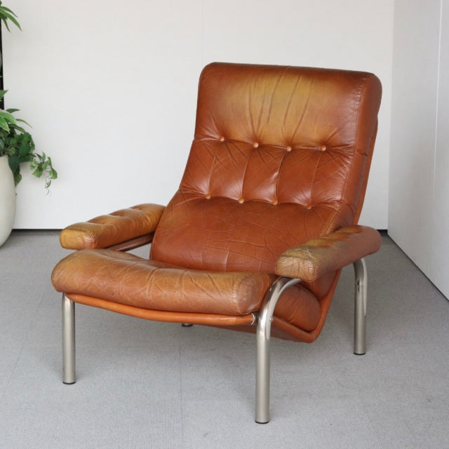 Vintage mid-century British leather lounge chair with tufted brown leather upholstery, curved teak armrests, and metal legs, .