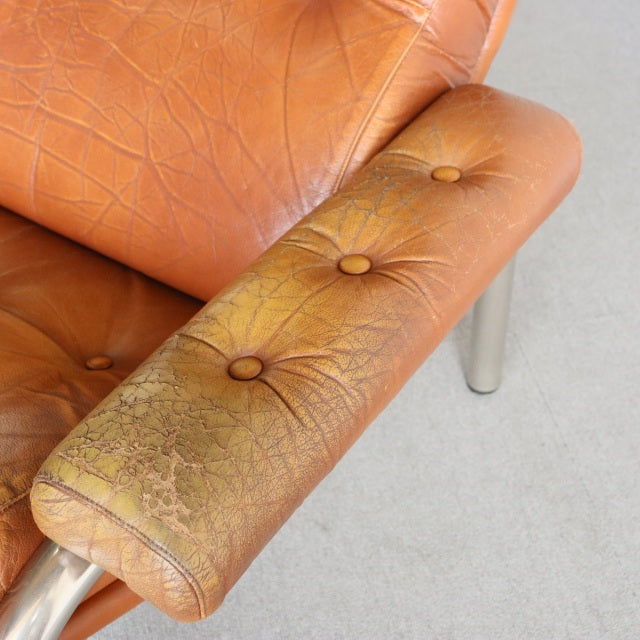 Close-up of vintage British mid-century leather sofa armrest with weathered teak wood grain and button tufting.