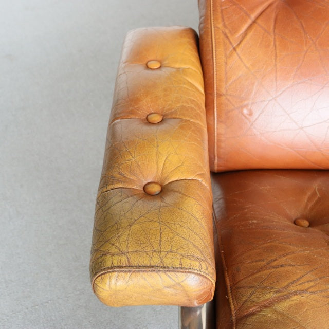 Mid-century British vintage sofa armrest in aged teak leather with button tufting and natural grain texture.