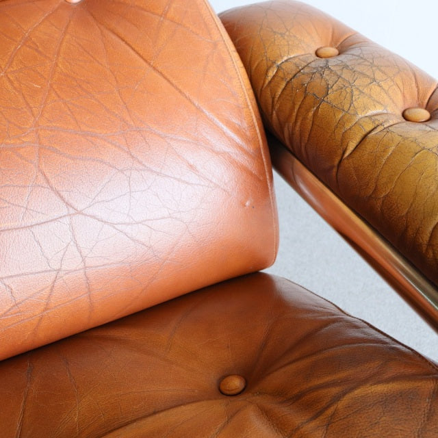 Close-up of vintage British mid-century sofa with worn brown leather cushions and visible teak wood frame grain.