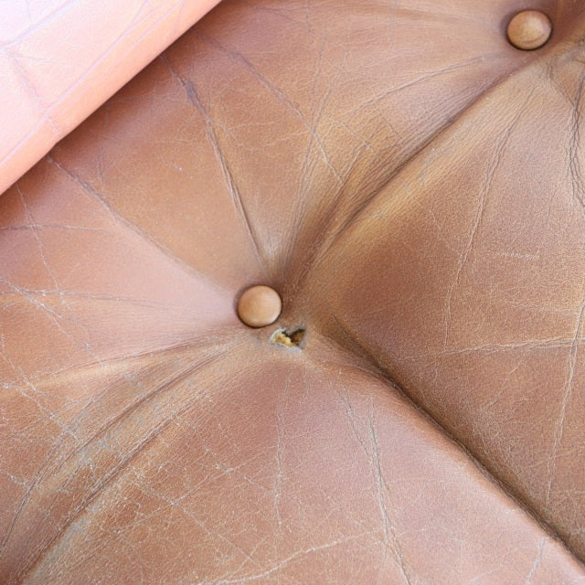 Close-up of vintage British mid-century leather sofa cushion with visible natural creases and button tufting.