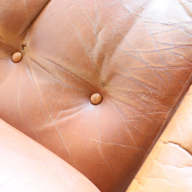 Close-up of vintage British mid-century sofa with worn tan leather upholstery and deep button tufting.