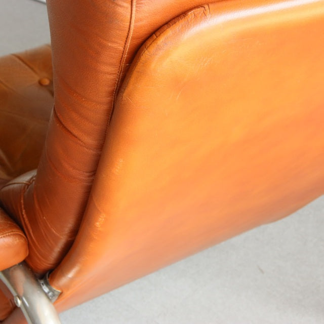 Mid-century British vintage sofa in smooth teak leather with sleek curved back and polished wooden legs.