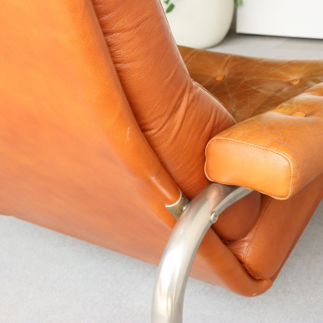 Mid-century vintage British sofa with rich caramel leather and polished teak legs, smooth grain visible.