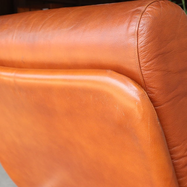 Close-up of vintage British mid-century sofa with smooth teak wood grain and caramel-brown leather upholstery detailing.