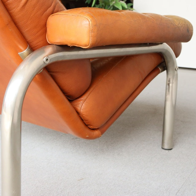 Vintage mid-century sofa with rich teak wood grain, tan leather cushions, and sleek curved metal legs in British-Denmark.