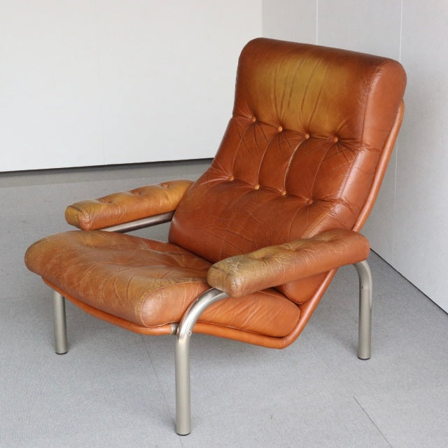 Vintage mid-century lounge chair with rich teak leather upholstery, button tufting, and sleek tubular metal legs,.