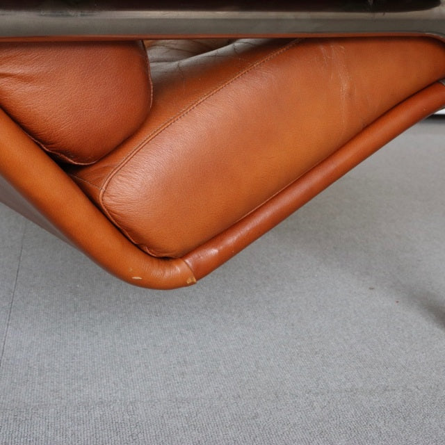 Close-up of vintage British mid-century teak sofa corner with smooth tan leather upholstery and visible wood grain legs.