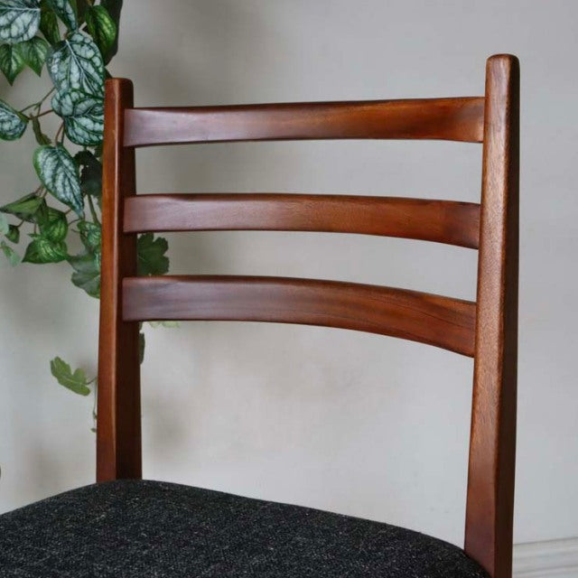 Set of four vintage mid-century teak dining chairs with curved slatted backs, smooth wood grain, and dark upholstered seats, .
