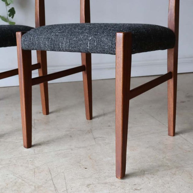 Set of four vintage teak mid-century British dining chairs with dark gray upholstered seats and slender angled legs.