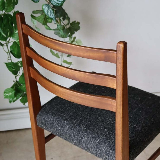 Mid-century vintage teak dining chair with British design, ladder back, dark fabric seat, smooth wood grain, straight legs.