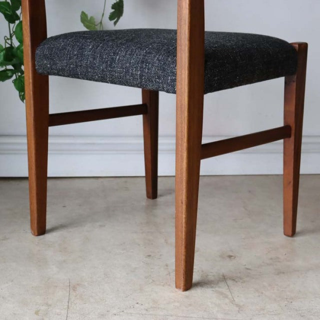 Mid-century British vintage teak dining chair leg detail with dark grey upholstered seat and slender tapered legs.