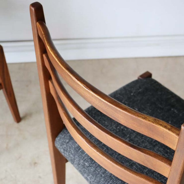 Set of four vintage mid-century British teak dining chairs with ladder-back design and dark fabric seats.