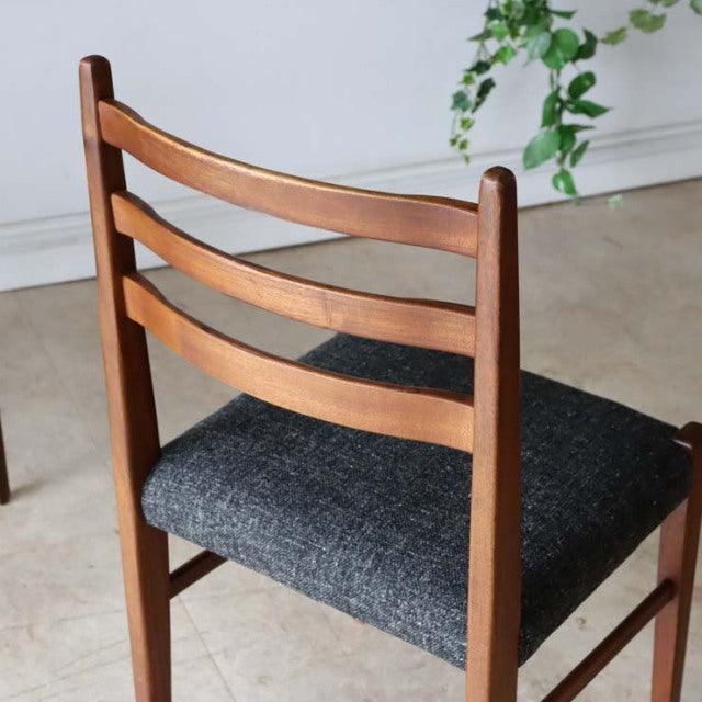 Set of four vintage British mid-century teak dining chairs with curved slat backrests and dark gray fabric seats, showcasing .