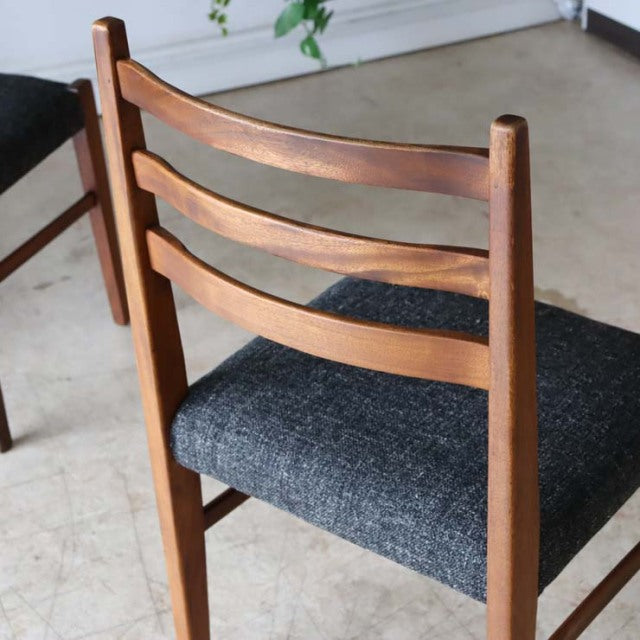 Set of four vintage British mid-century teak dining chairs with dark gray upholstered seats and solid wood frames showing.