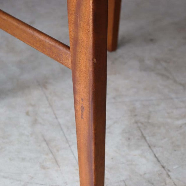 Close-up of vintage teak dining chair leg with smooth grain and warm mid-century finish on concrete floor.