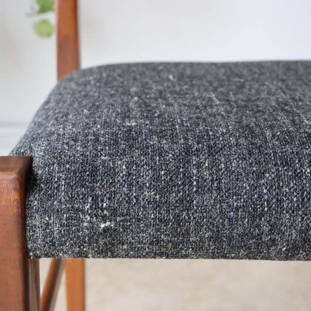 Close-up of vintage British mid-century teak dining chair seat with textured dark gray fabric upholstery and visible wood.
