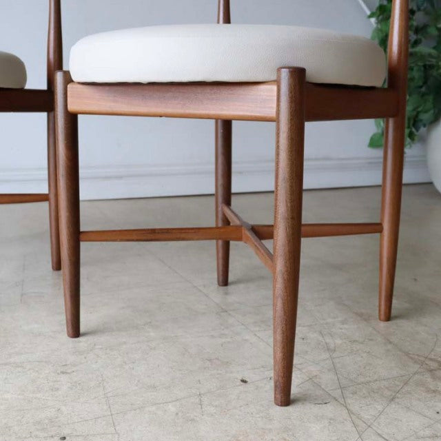 Pair of British vintage mid-century teak dining chairs with gently tapered legs and cream upholstered seats.