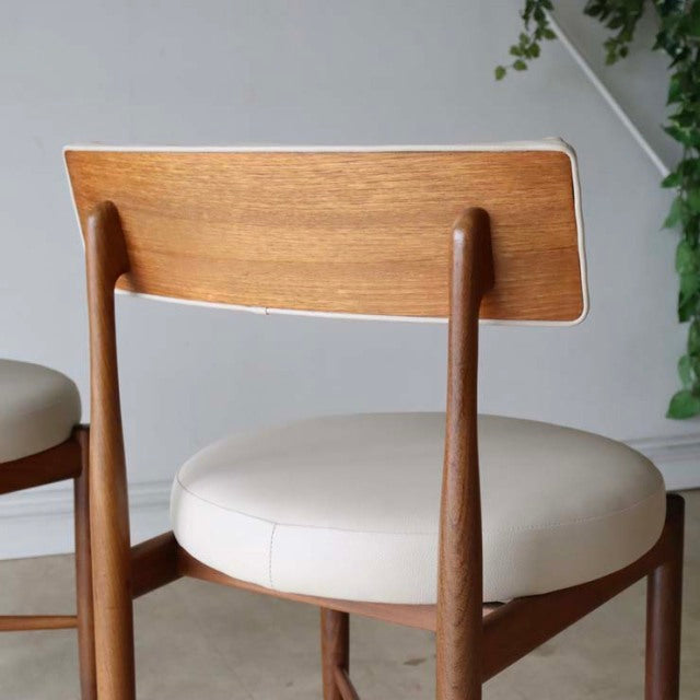 Set of two British vintage mid-century dining chairs in teak with cream round cushioned seats and slender angled legs.