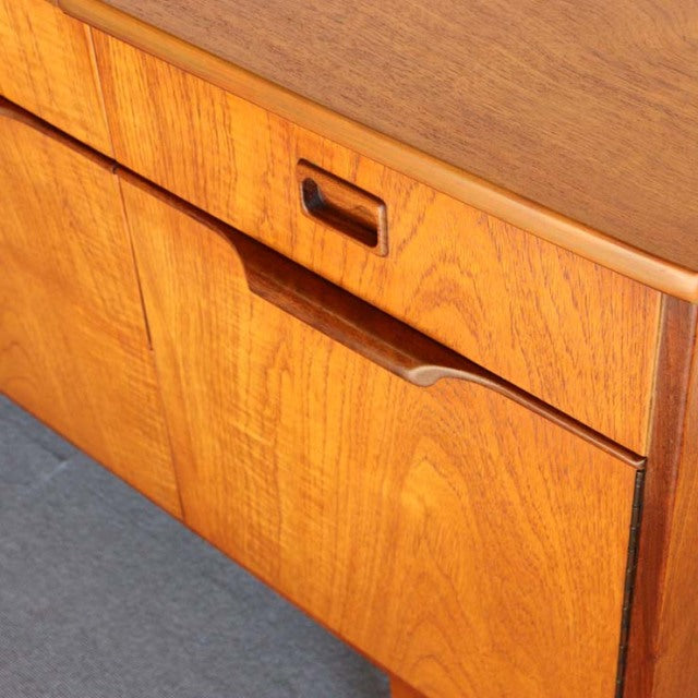 Mid-century British vintage teak sideboard with rich wood grain and recessed handles, smooth finish.