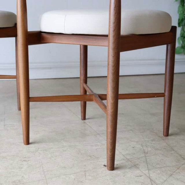 Set of two vintage British G-plan mid-century teak dining chairs with tapered legs and natural wood grain, featuring cream.