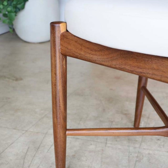 Close-up of mid-century vintage British teak dining chair leg with smooth wood grain and light beige upholstered seat.