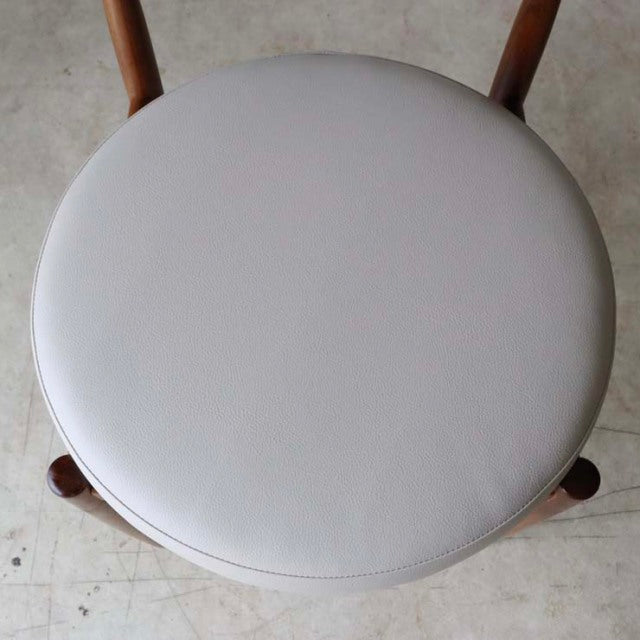 Vintage G-plan mid-century teak dining chair with round light gray leather seat, slender wooden legs.