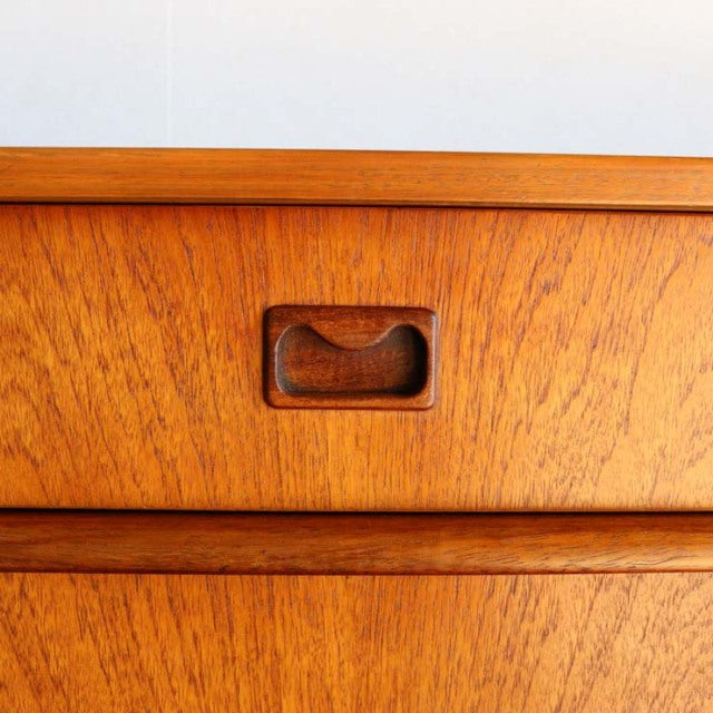 Close-up of vintage teak sideboard drawer front with carved recessed handle and warm wood grain from British mid-century.