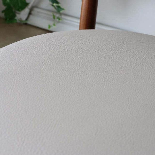 Close-up of beige textured upholstery on vintage mid-century teak dining chair seat with visible wood grain on backrest leg, .