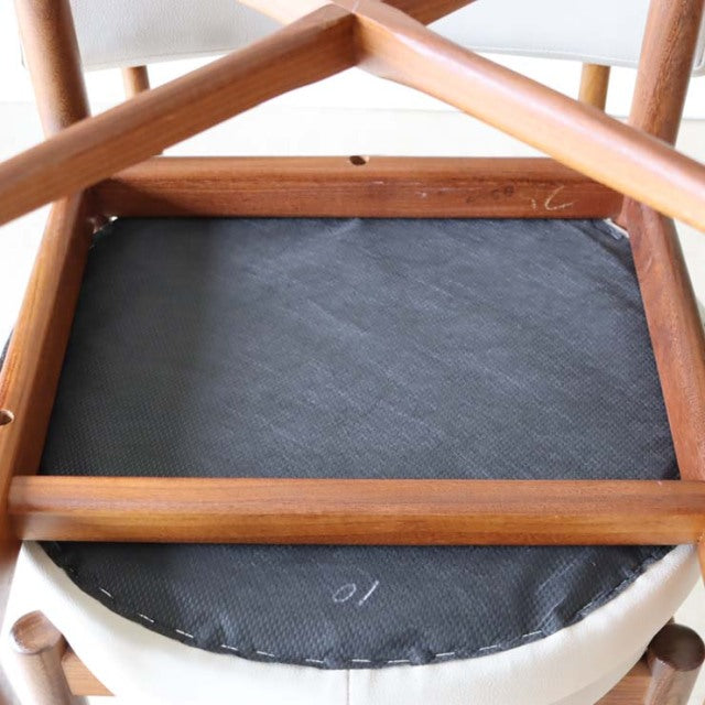 Underside view of two teak British mid-century G-Plan dining chairs showing wood grain frame and black seat backing.
