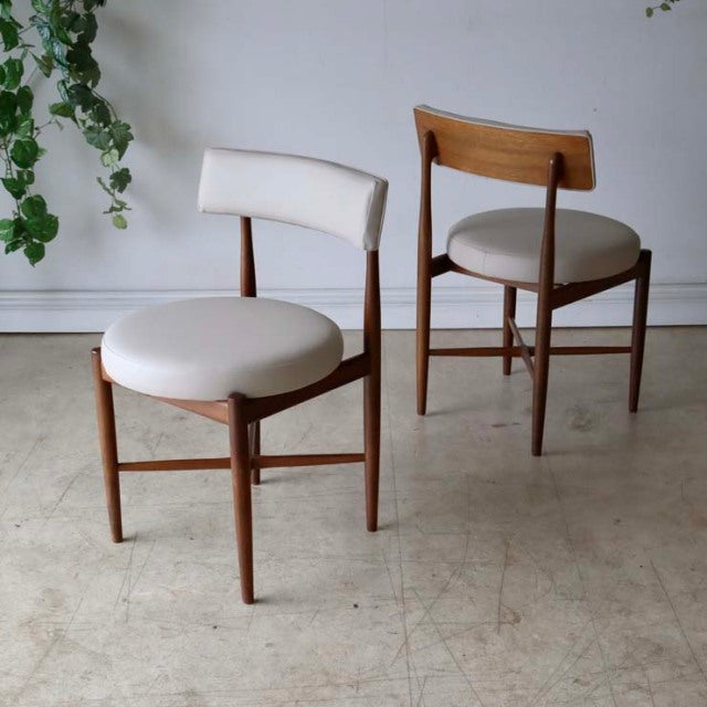 Pair of vintage G-Plan mid-century teak dining chairs with rounded cream upholstered seats and curved backrests, showcasing.