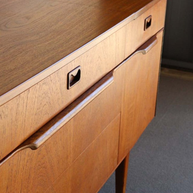 Mid-century British vintage teak sideboard with rich wood grain, recessed handles, and slender tapered legs.