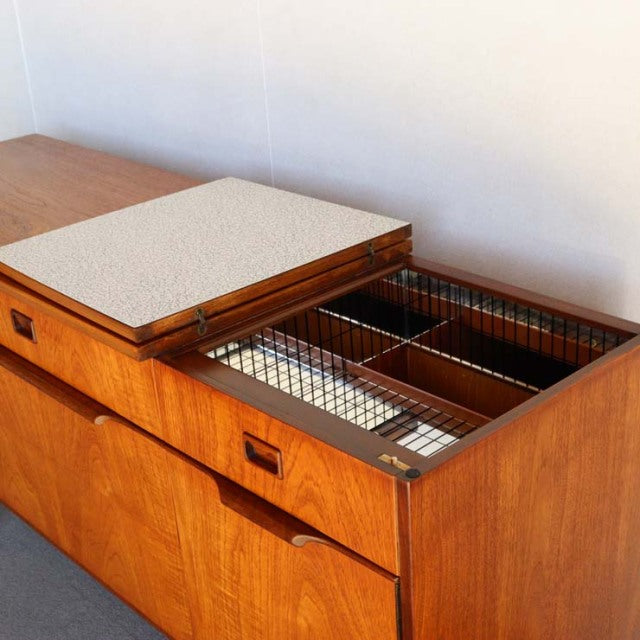 Mid-century British vintage teak sideboard with smooth wood grain, recessed handles, and open top compartment with metal.