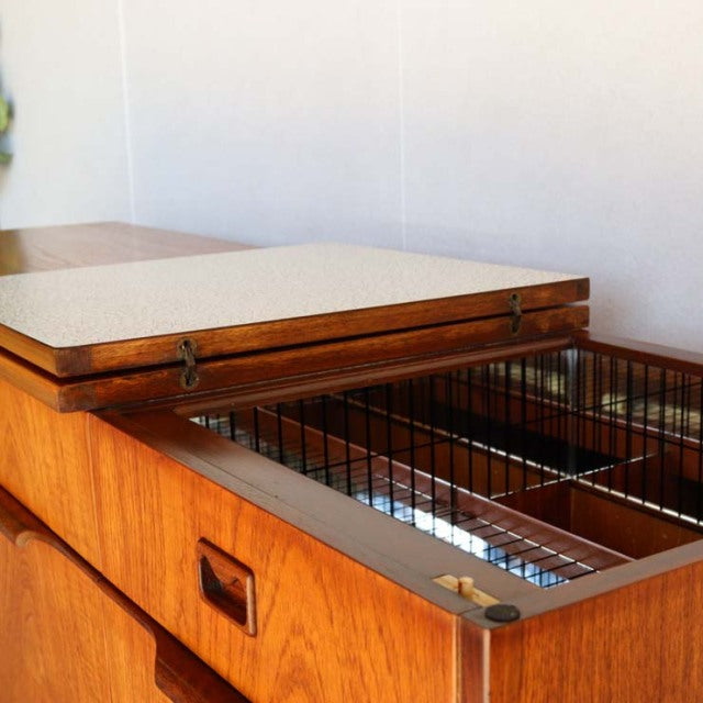 Vintage teak mid-century British sideboard with rich wood grain, metal wire baskets, and recessed handles.