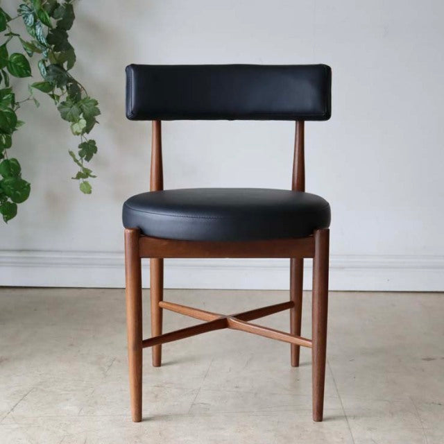 Set of four vintage British G-Plan mid-century dining chairs in teak with black leather seats and low backrests, showcasing.
