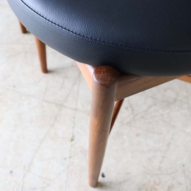 Mid-century British G-plan teak dining chair leg with smooth grain and black leather seat corner.