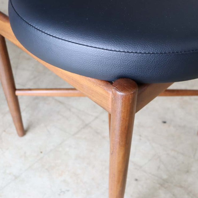 Close-up of British mid-century G-Plan vintage teak dining chair leg with smooth wood grain and black leather seat cushion.