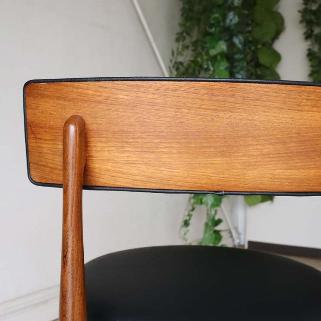 Close-up of vintage British G-PLAN teak dining chair backrest with visible wood grain and curved top rail against a neutral.