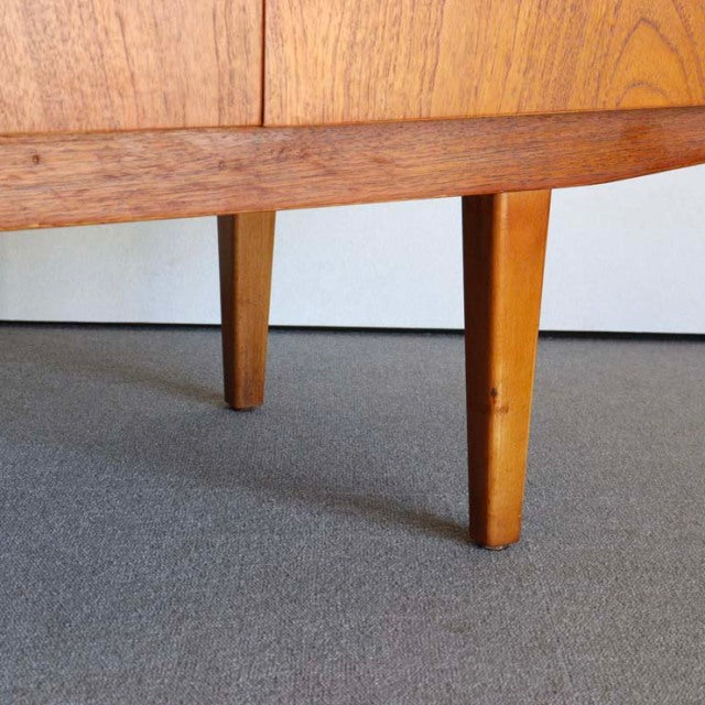 Mid-century British vintage teak sideboard legs with tapered design and warm wood grain finish on gray carpet.