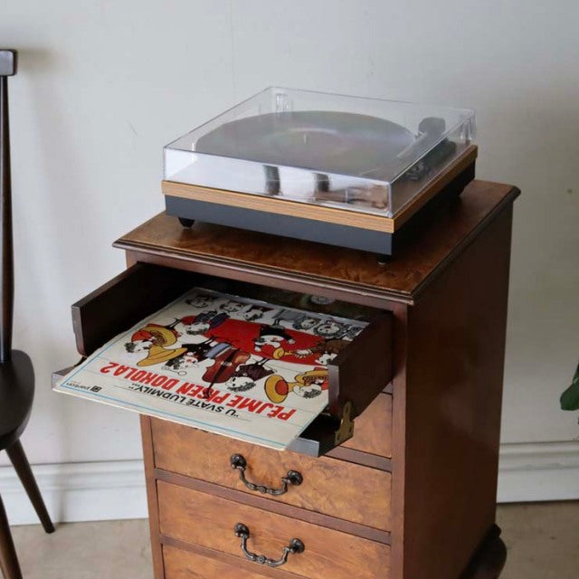 British mid-century teak record cabinet with rich wood grain, three drawers, metal handles, and a vintage turntable on top.