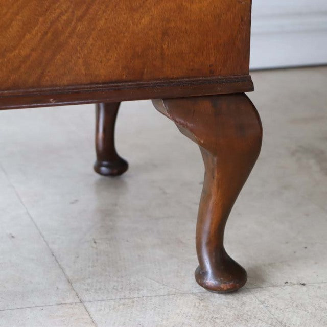 Close-up of mid-century British vintage teak cabinet leg with elegant curved shape and rich wood grain finish on light floor.