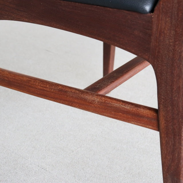 Close-up of vintage teak mid-century dining chair leg with smooth wood grain and black leather seat from Younger Fonseca.